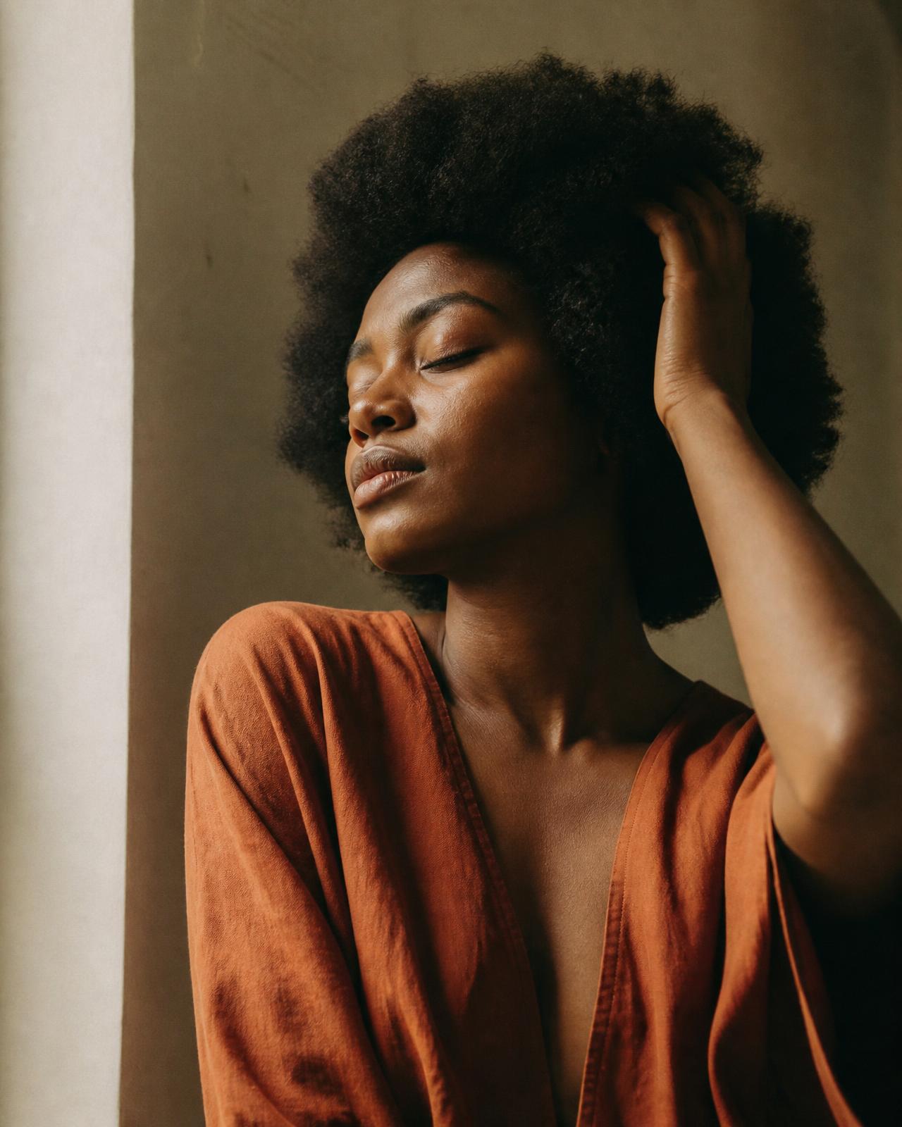 A Black woman with a natural afro, eyes closed, hand resting in her hair